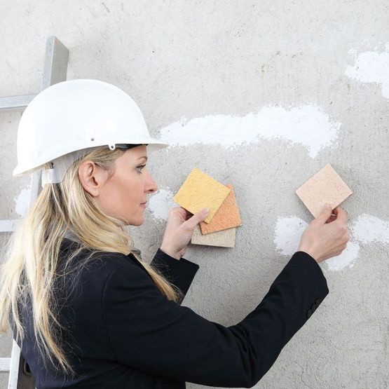mujer con casco de seguridad coloca muestras d ecolor en pared de cemento
